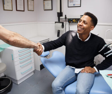 Young African-American man shaking hand of crop dentist having visit in medical clinic.