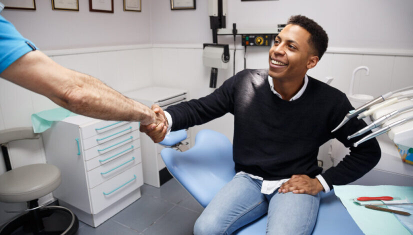 Young African-American man shaking hand of crop dentist having visit in medical clinic.